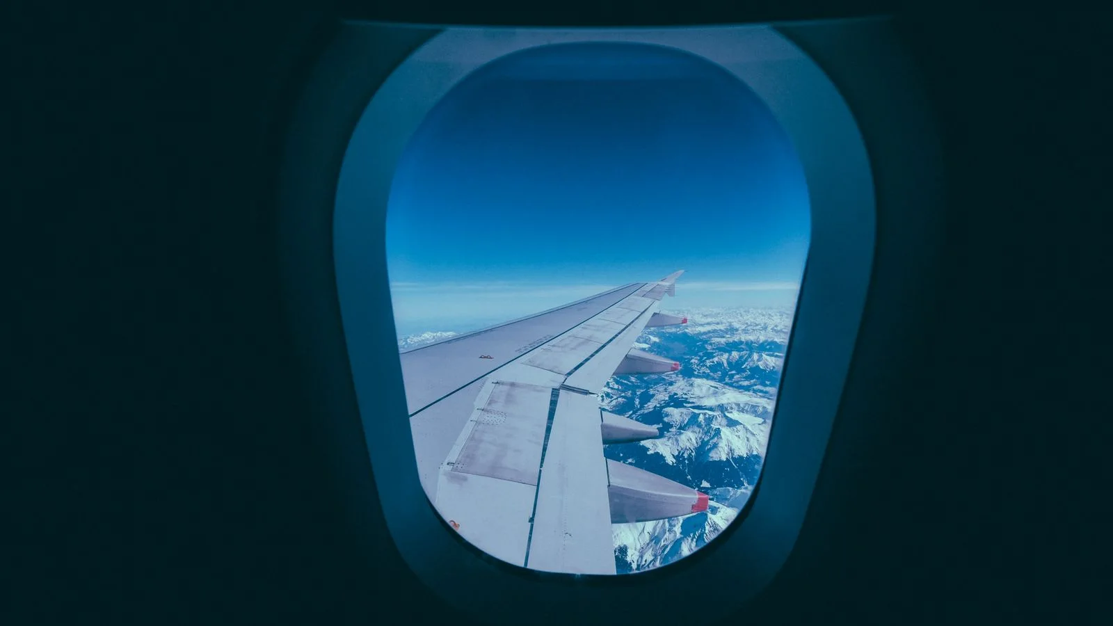 Vista da asa do avião e de montanhas nevadas pela janela, ilustrando viagem com milhas aéreas