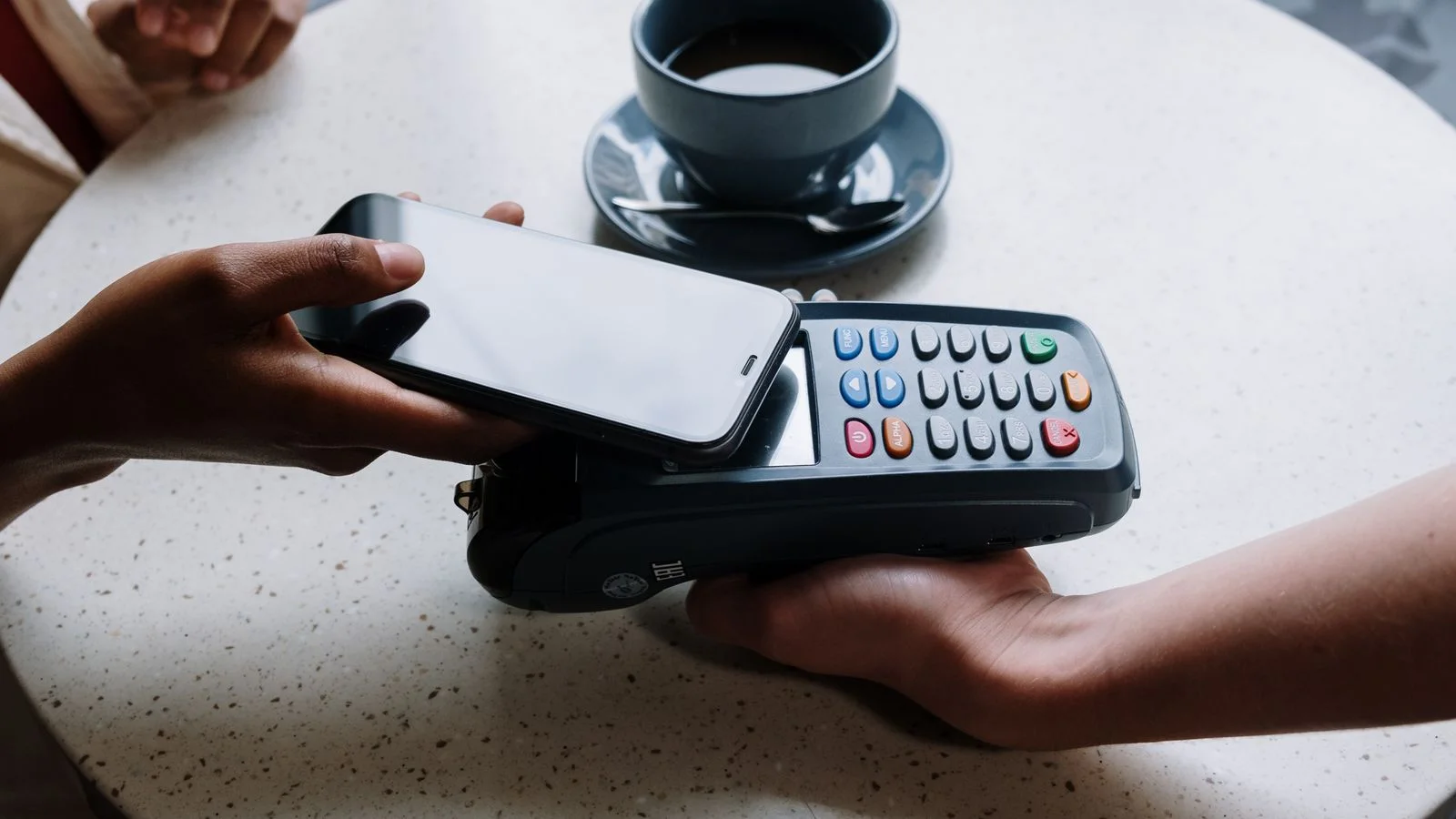 Pessoa usando smartphone para fazer pagamento em maquininha sobre a mesa de um café