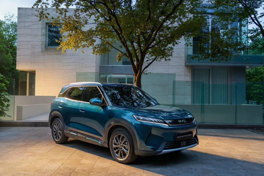 BYD Atto 2 DM-i azul estacionado em frente a uma casa moderna com árvore, visto de frente e de lado