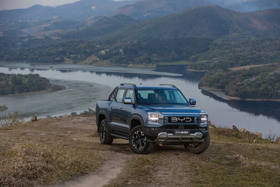 BYD Shark em estrada de terra no alto de um morro com represa e montanhas ao fundo
