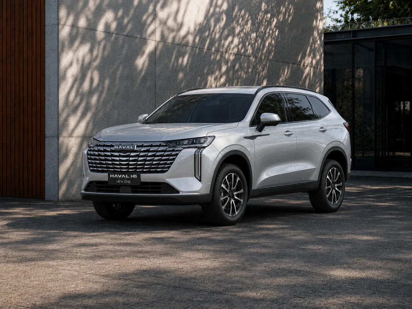GWM Haval H6 HEV One prata estacionado em frente a uma parede de pedra, visto de frente em ângulo de três quartos