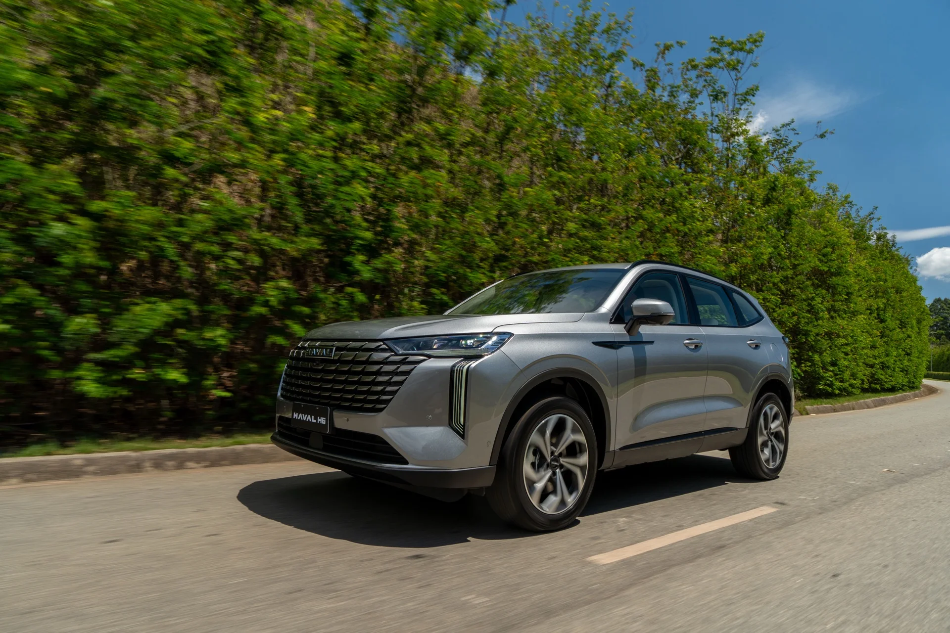 GWM Haval H6 PHEV35 Flex cinza rodando em uma estrada com vegetação ao fundo